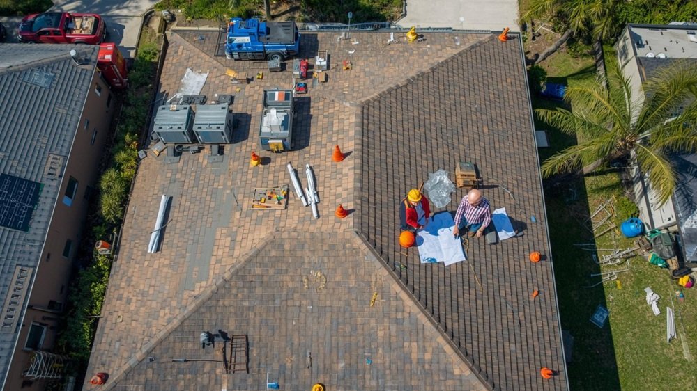 A vibrant aerial view of a professional residential roof replacement in Florida, showing a neat construction site with safety equipment and a licensed contractor reviewing blueprints with a homeowner.