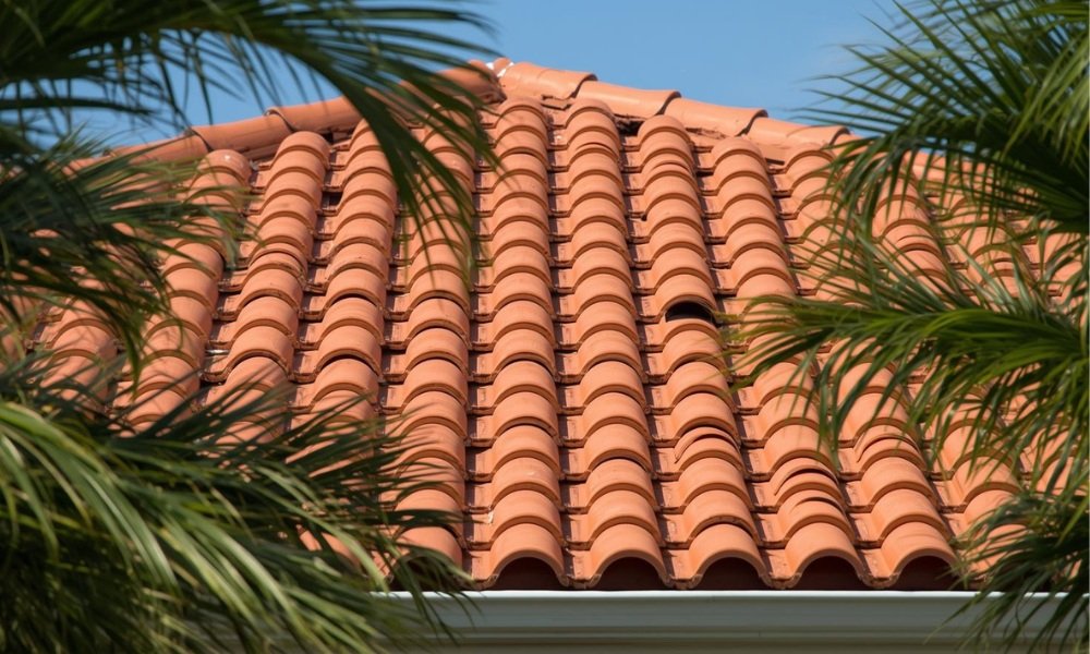A detailed photograph of a pristine concrete barrel tile roof on a modern South Florida home, emphasizing durability, thermal mass, and long-term energy efficiency under bright sunlight, framed by palm trees.