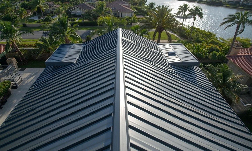 A majestic, high-angle architectural photograph capturing a high-end coastal home in Fort Lauderdale with a gleaming, recently installed standing seam metal roof. The intricate lines of the steel panels contrast against the background of palm trees, luxury properties, and a glimpse of the Intracoastal Waterway under clear sunlight, illustrating the cost guide topic.
